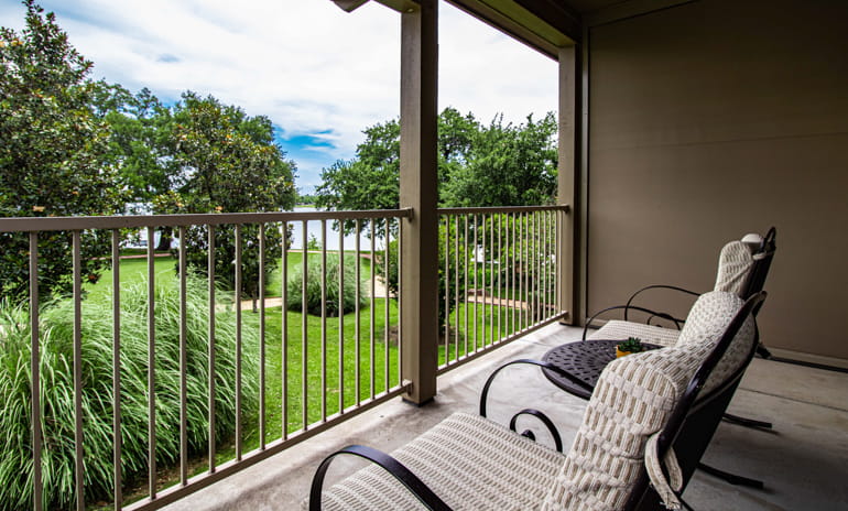 Private balcony with two chairs and a small table overlooking a grassy lawn and Lake Granbury beyond