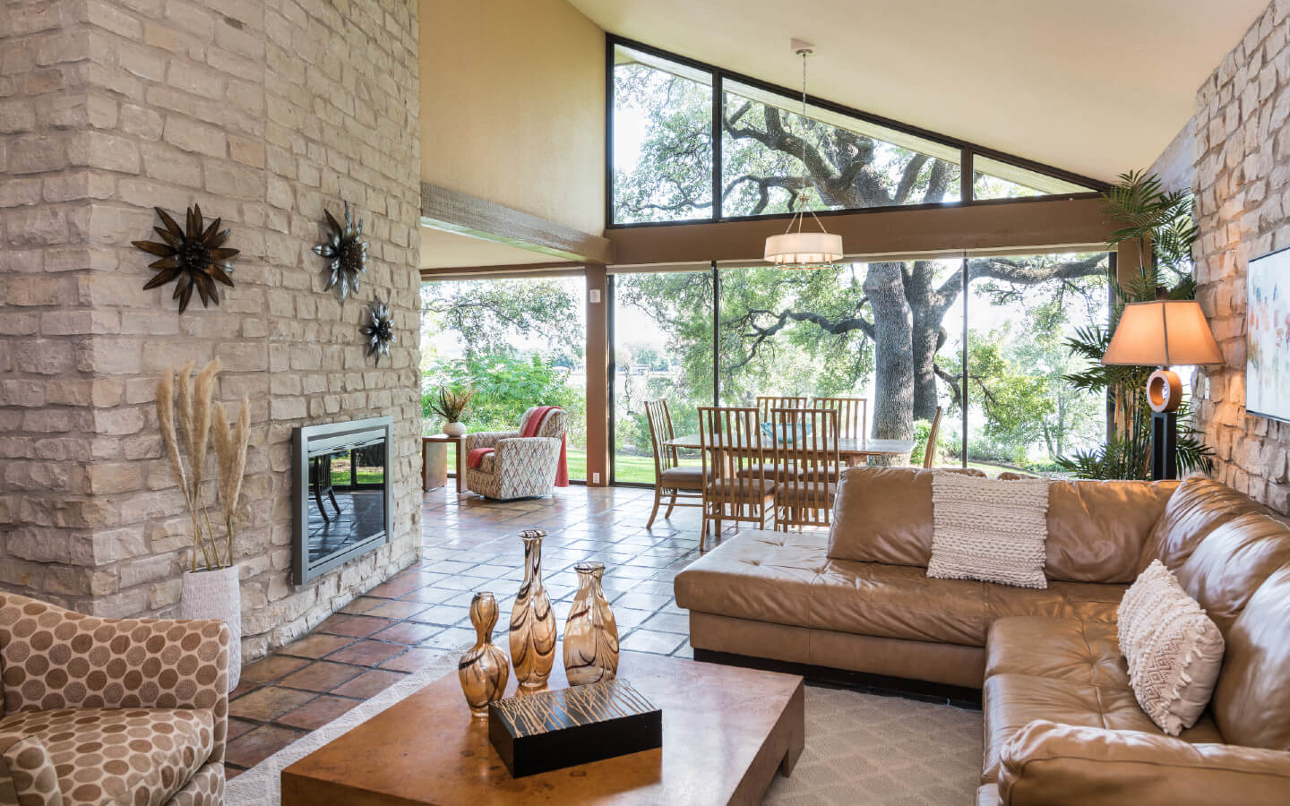 Sunny living room with tall sloped ceiling. Leather L-shaped sofa and coffee table accent sitting area across from brick fireplace.