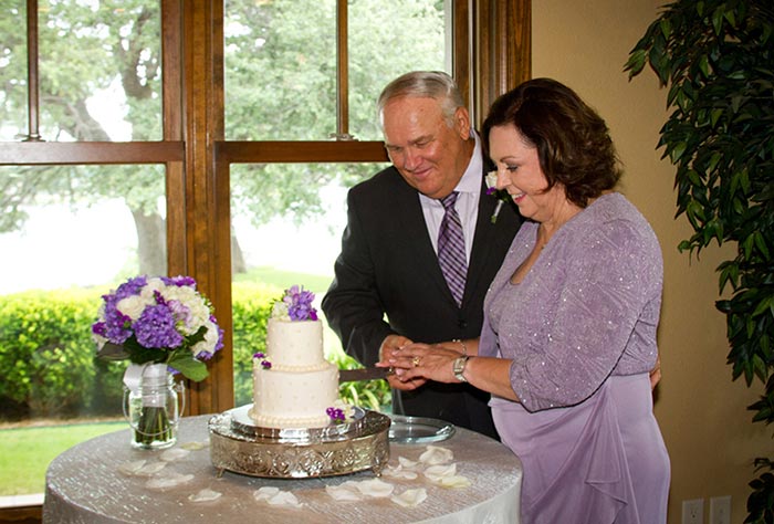 Couple looking at white wedding cake with purple flowers