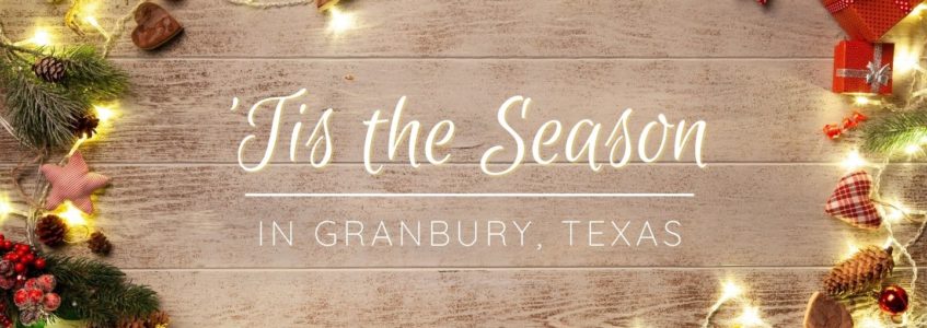 Wood board surrounded by twinkling Christmas lights that says: 'Tis the Season in Granbury, TX