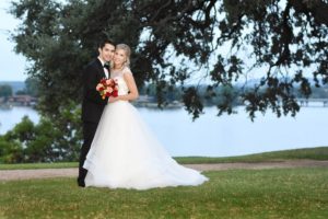 Bride and groom smiling in front of tree and lake