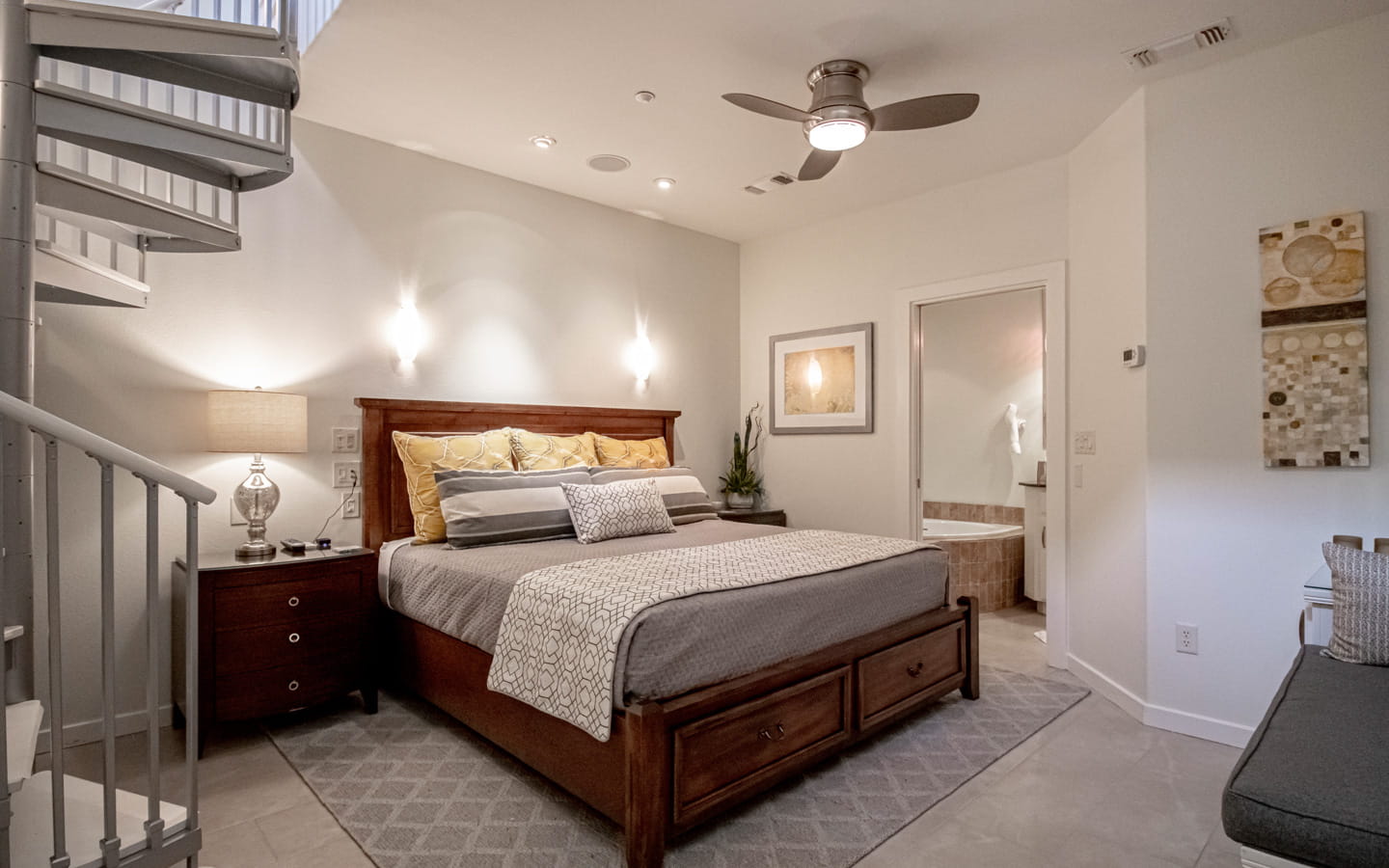 Queen storage bed with two end tables, a ceiling fan, and metal spiral staircase