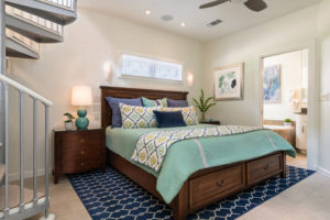 Spiral Staircase leading to bedroom with high back bed with blues, whites, and purples. Artwork on the walls and open door to bathroom.