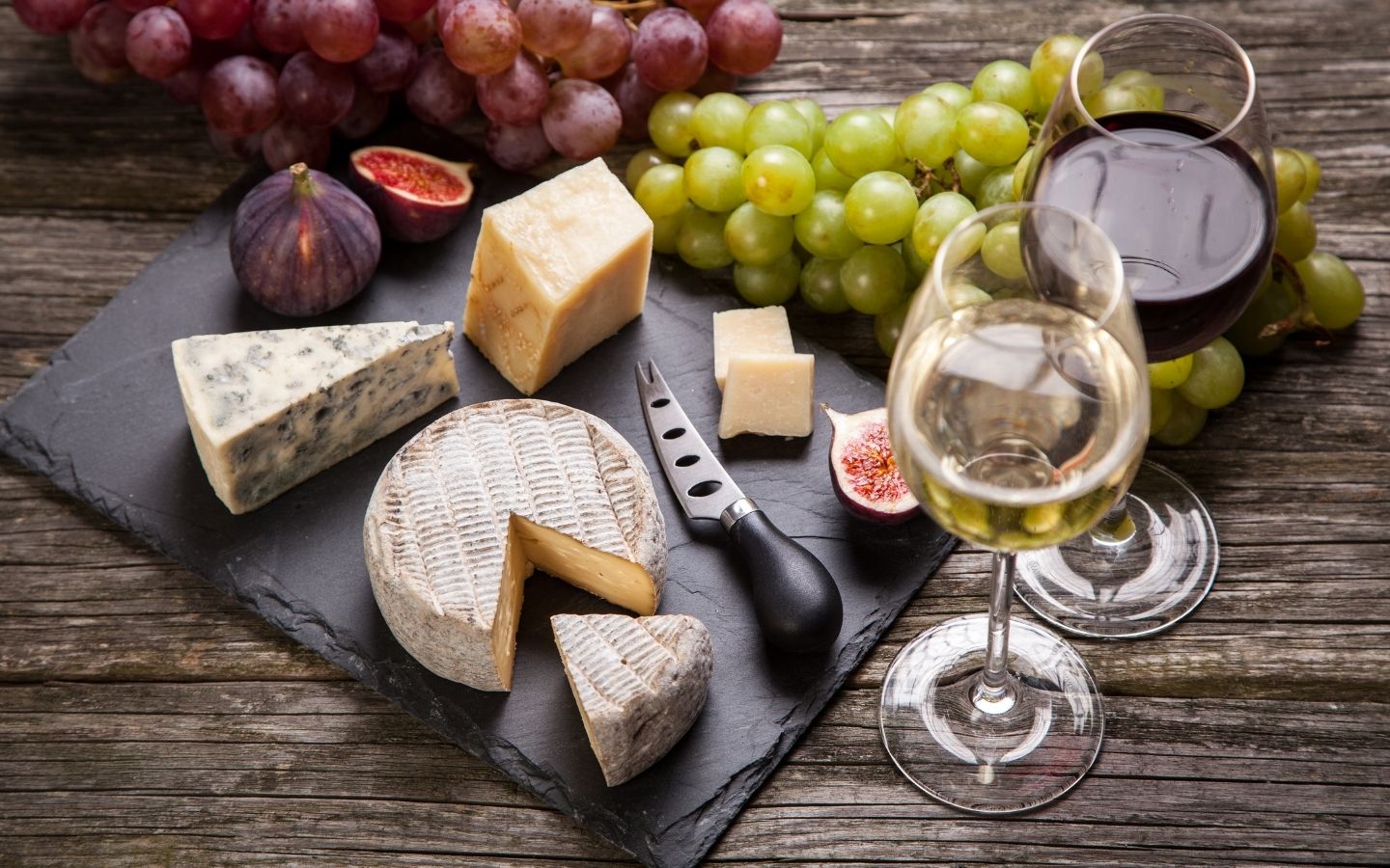 Red and green grapes, different types of cheese and two glasses of red and white wine