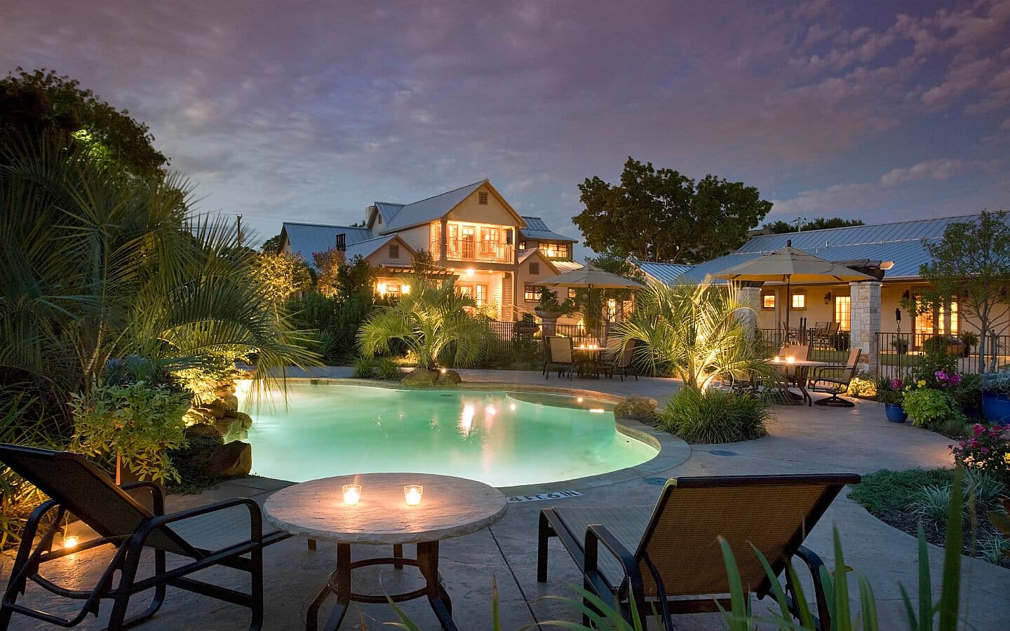 View of the lit up inground pool and inn at dusk