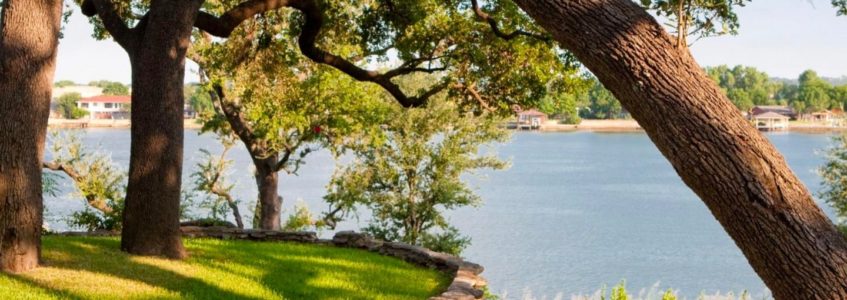 View of Lake Granbury through the trees beyond a stone-edged grassy bluff