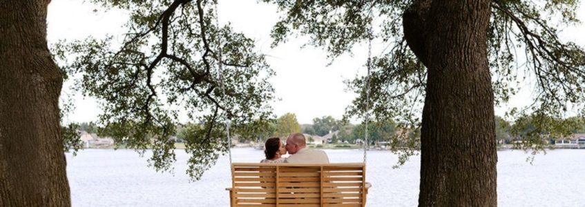 Bride and groom kissing on a swing between two oak trees by Lake Granbury