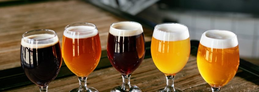 Table topped with 5 frothy beers in 5 different colors