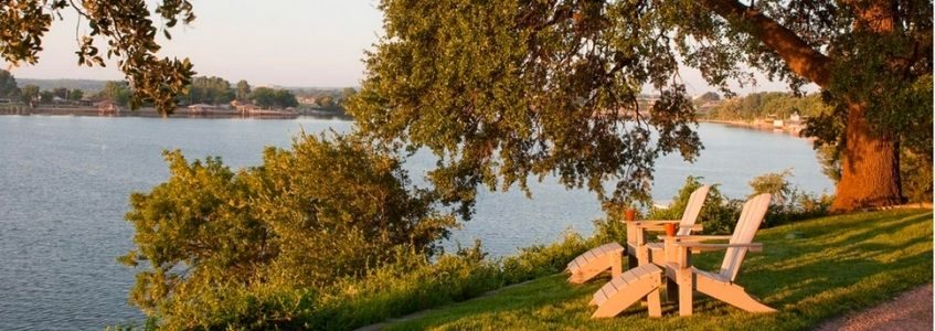 Two adirondack chairs on the grass under a big oak tree face Lake Granbury